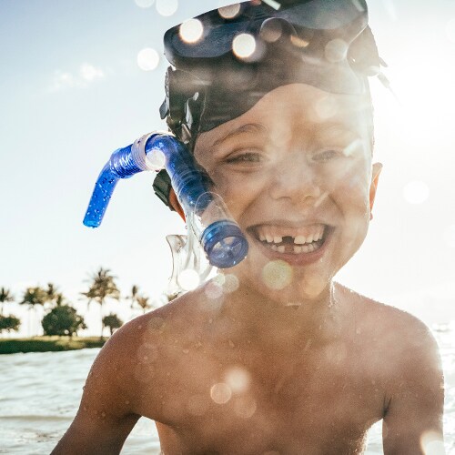 A smiling young boy in shallow ocean water, his snorkeling mask worn high on his forehead