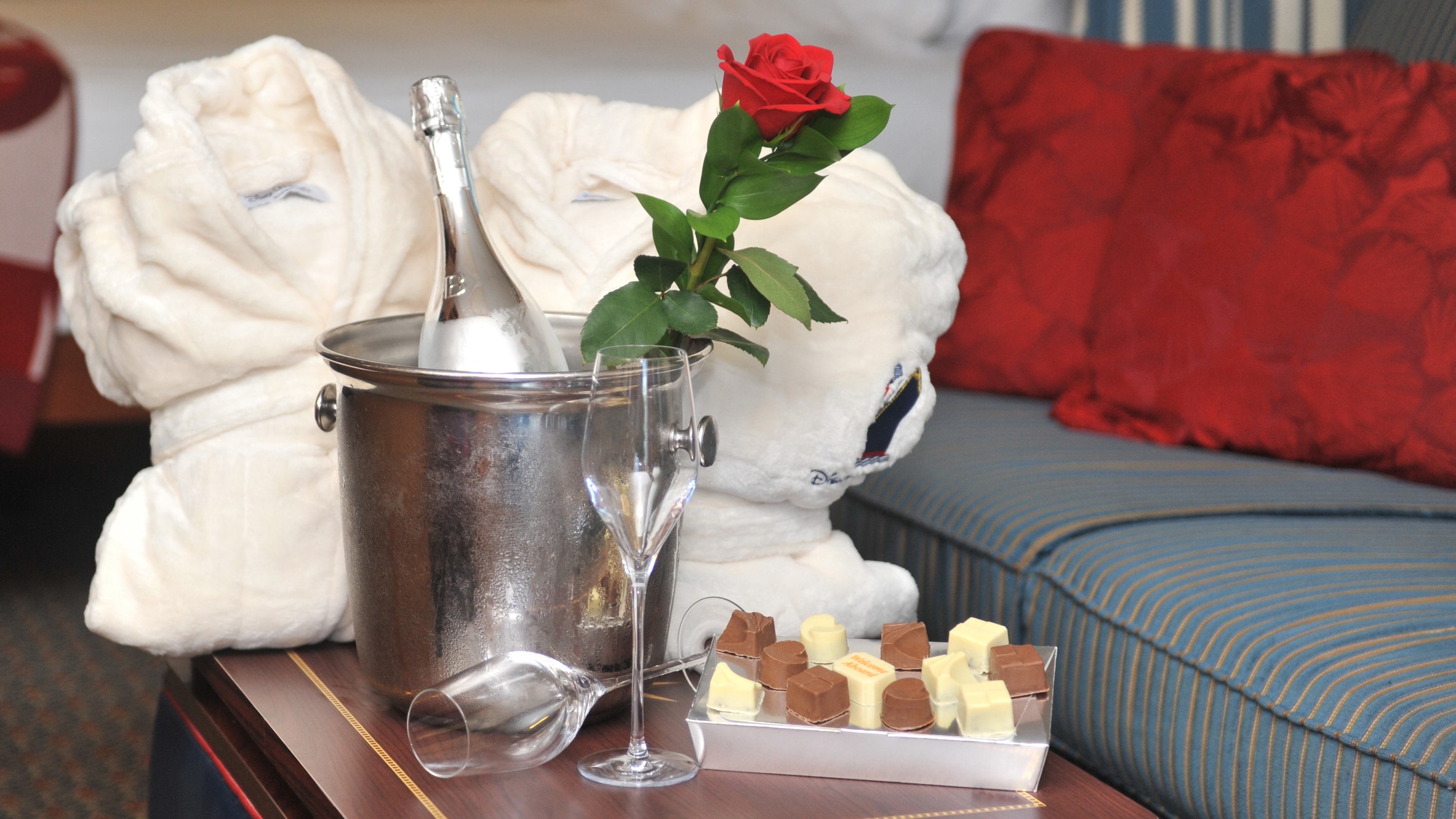 A box of chocolates, 2 bath robes and 2 glasses next to an ice bucket with a rose and a bottle of Champagne