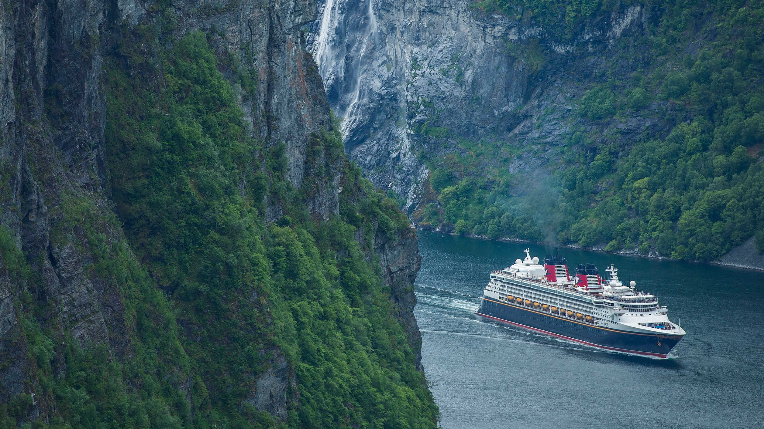 A Disney cruise ship sailing between 2 steep mountains