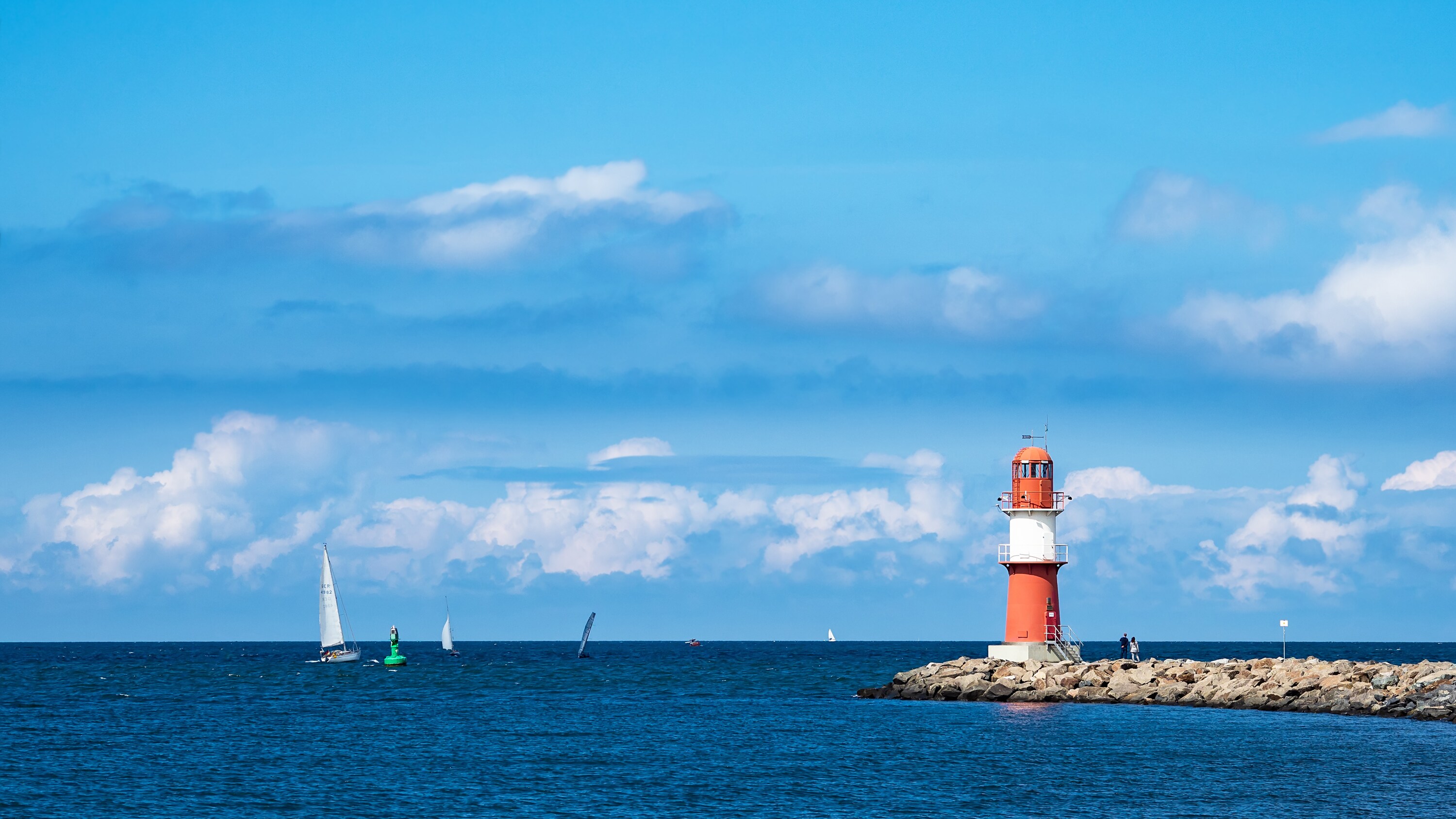 Sailboats sailing near a lighthouse on the water's edge