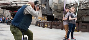 A couple holding lightsabers poses for a photographer in front of the Millennium Falcon.