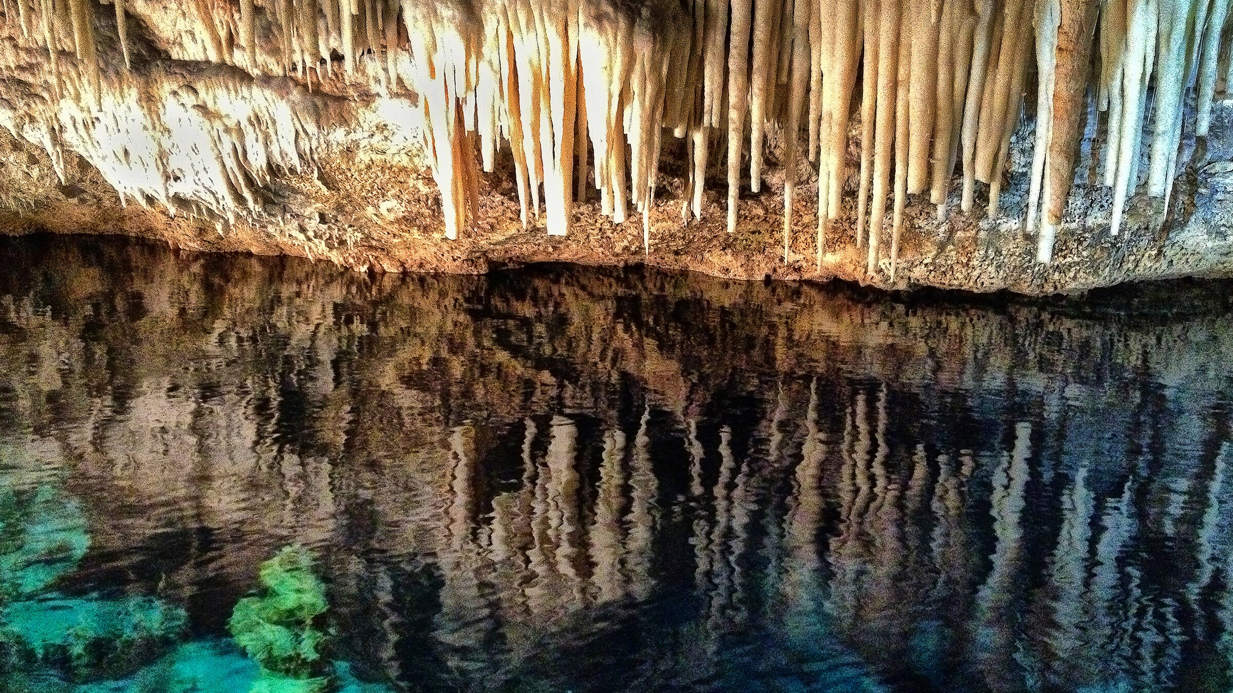 Stalactites hang over a pool of water in a cave