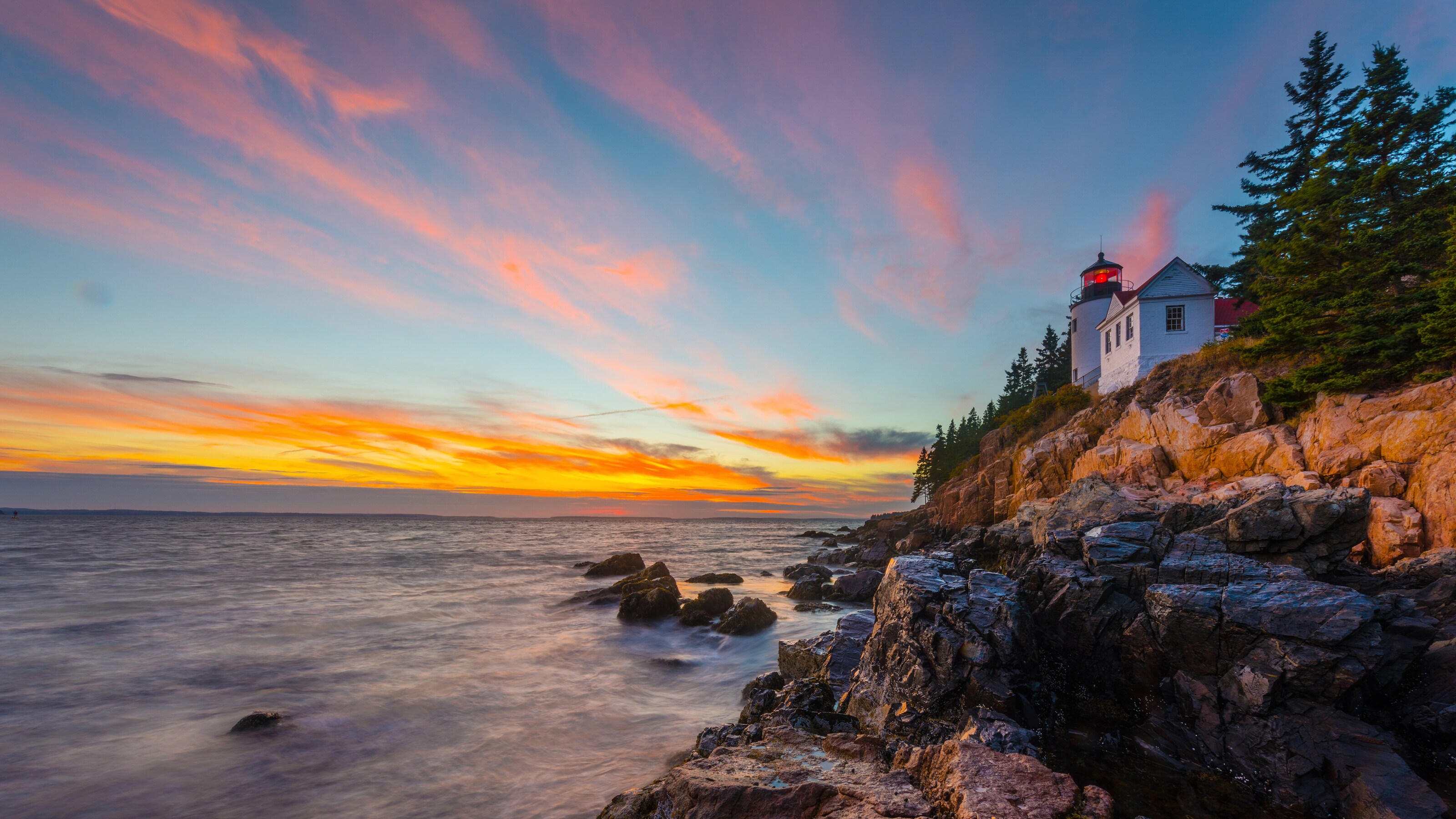 A lighthouse by the ocean on the edge of a rocky cliff featuring trees