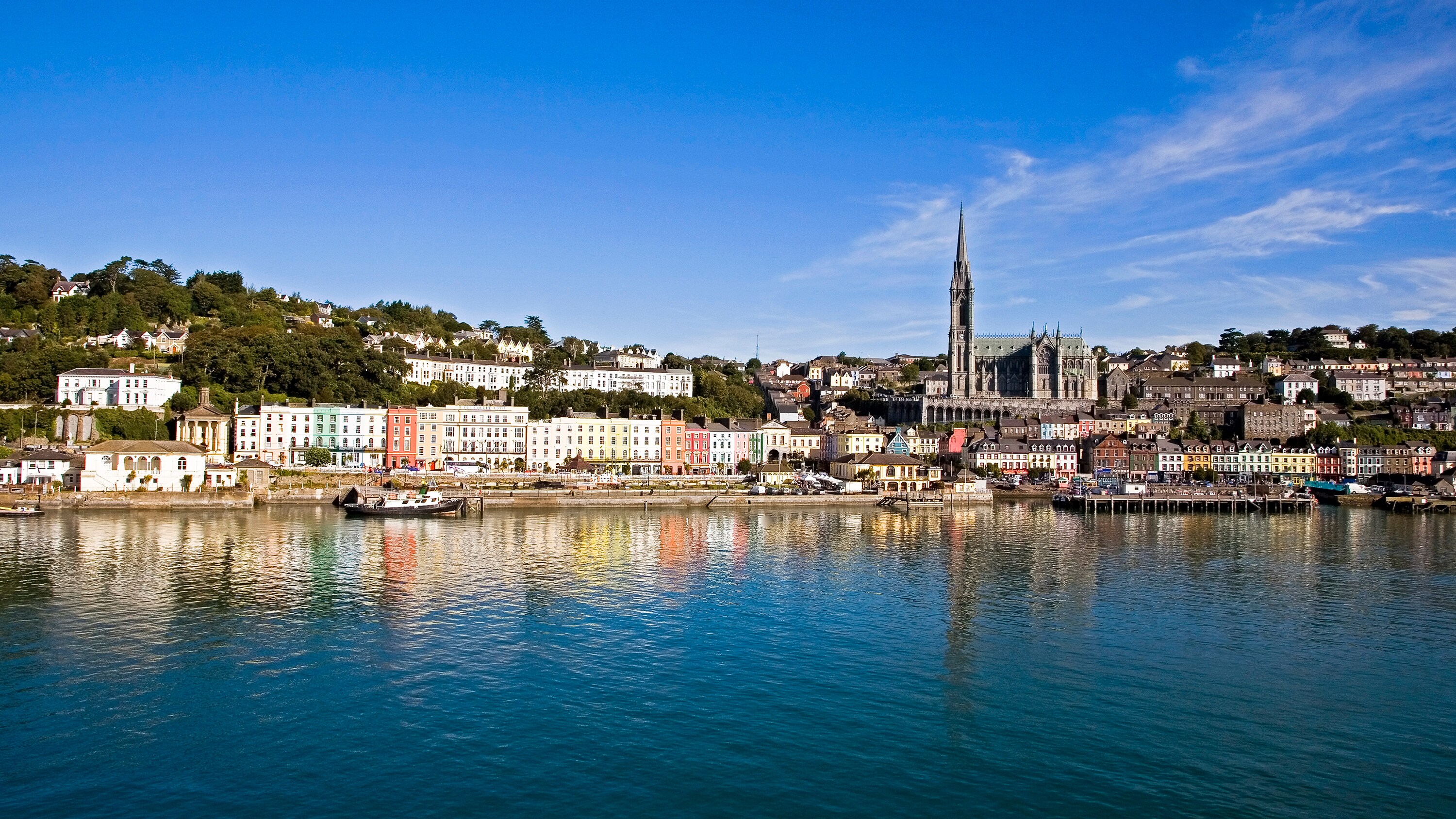 Cobh Harbor in Cork, featuring a serene marina, a row of houses and the Church of the Holy Rosary cathedral