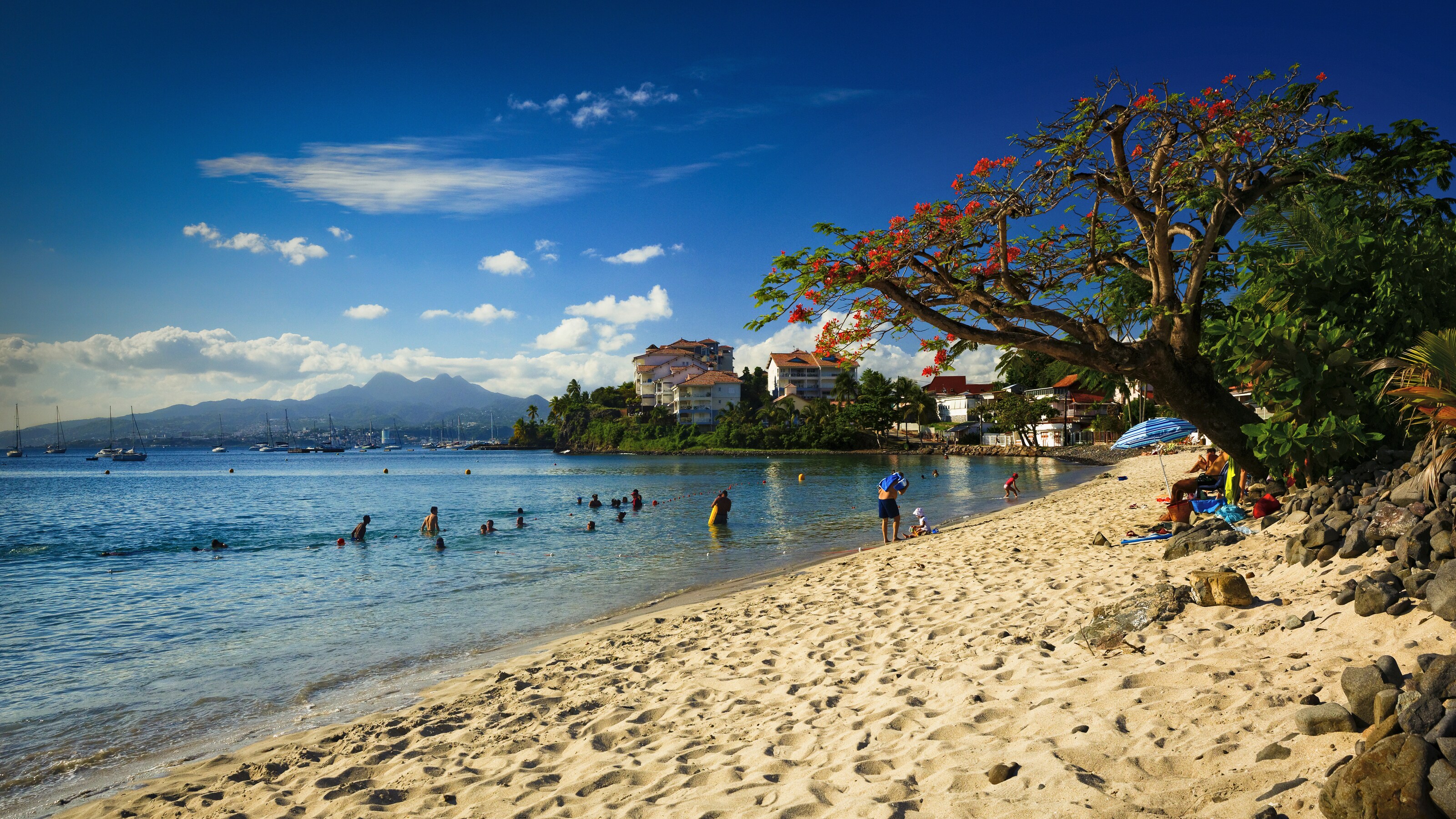 People wading in the waters of a beach in front of an old French village