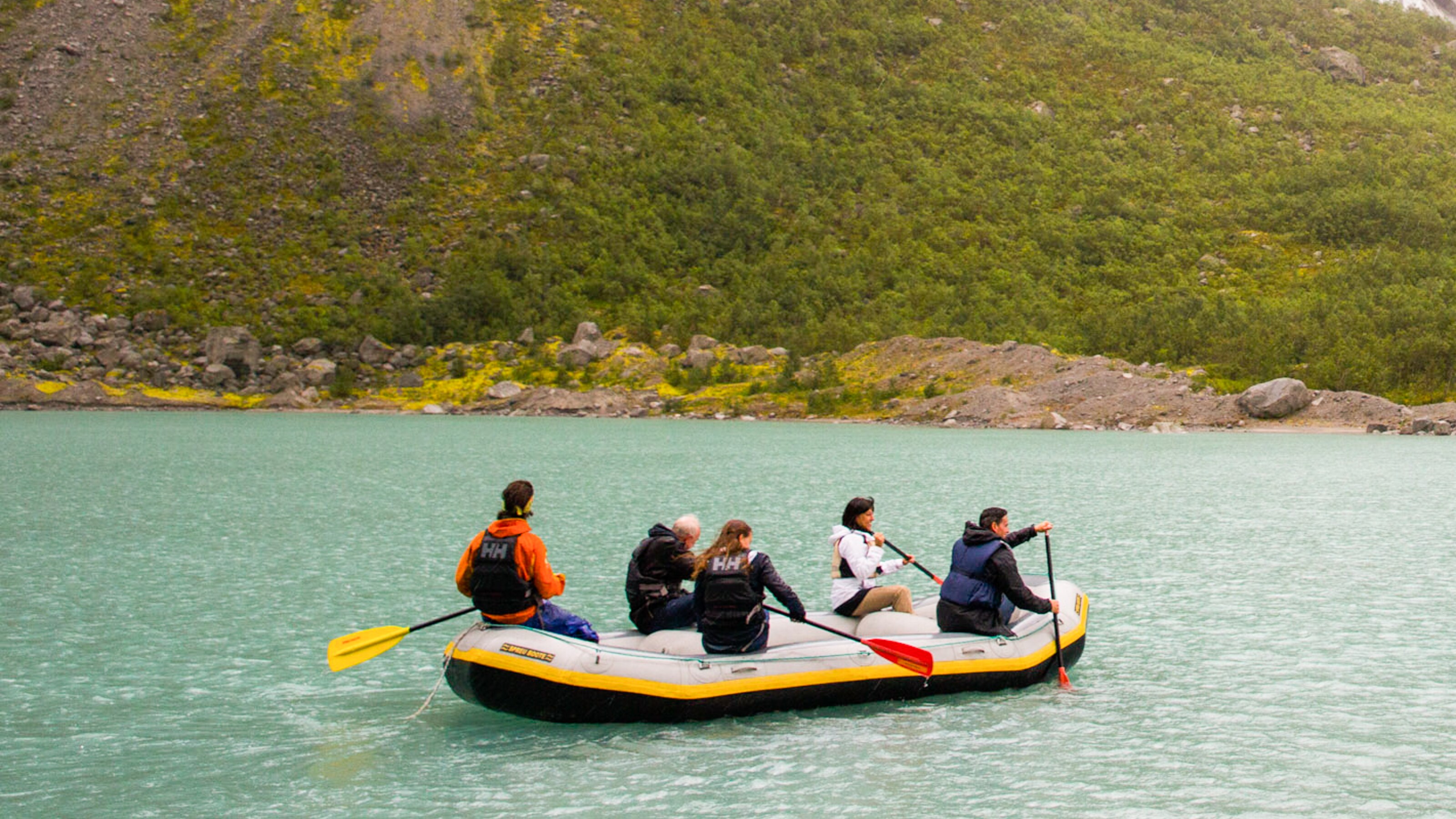 Five people paddling in an inflatable raft with a hillside in the background