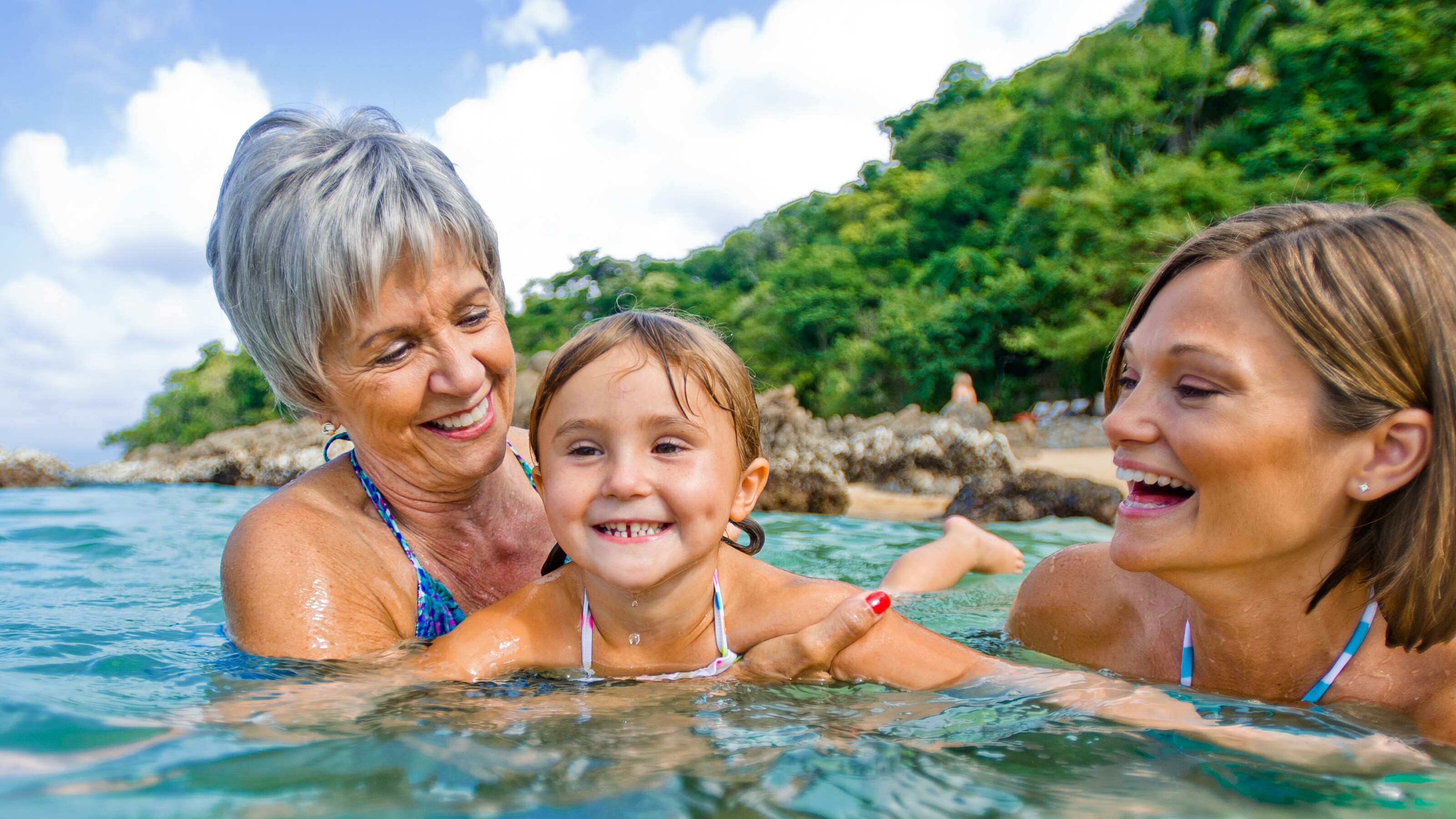 Little girl smiling while being held by an older woman in the ocean
