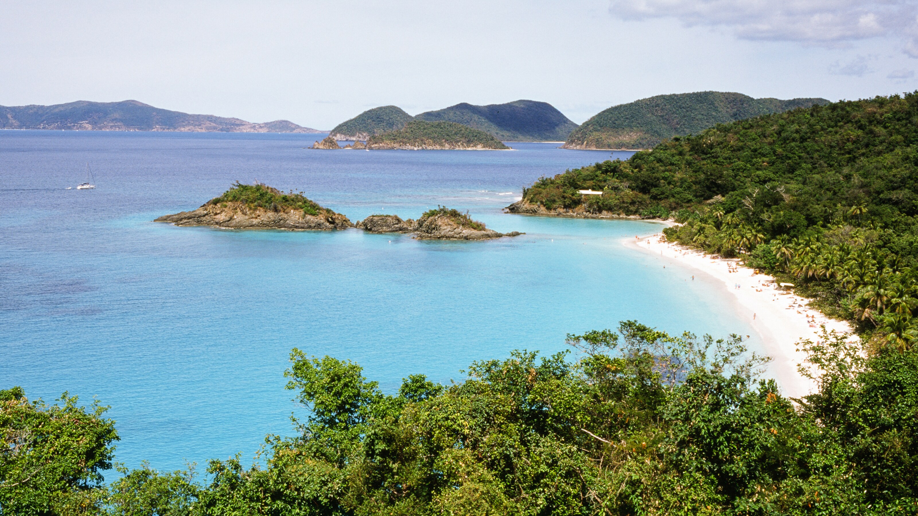 Aerial shot of a bay with several islands covered in plants and a beach in the foreground