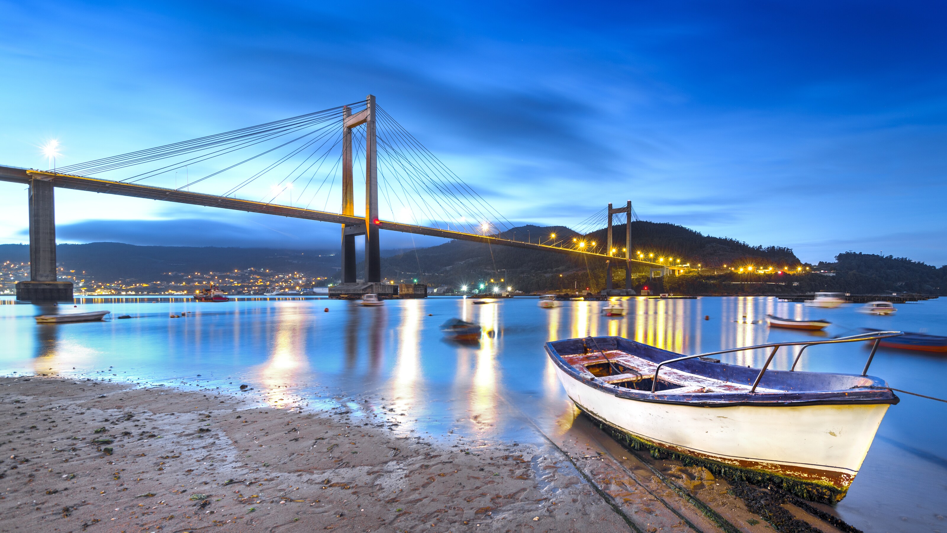 A boat sits in muddy drydock, with the Rande Bridge behind it, in Vigo Spain