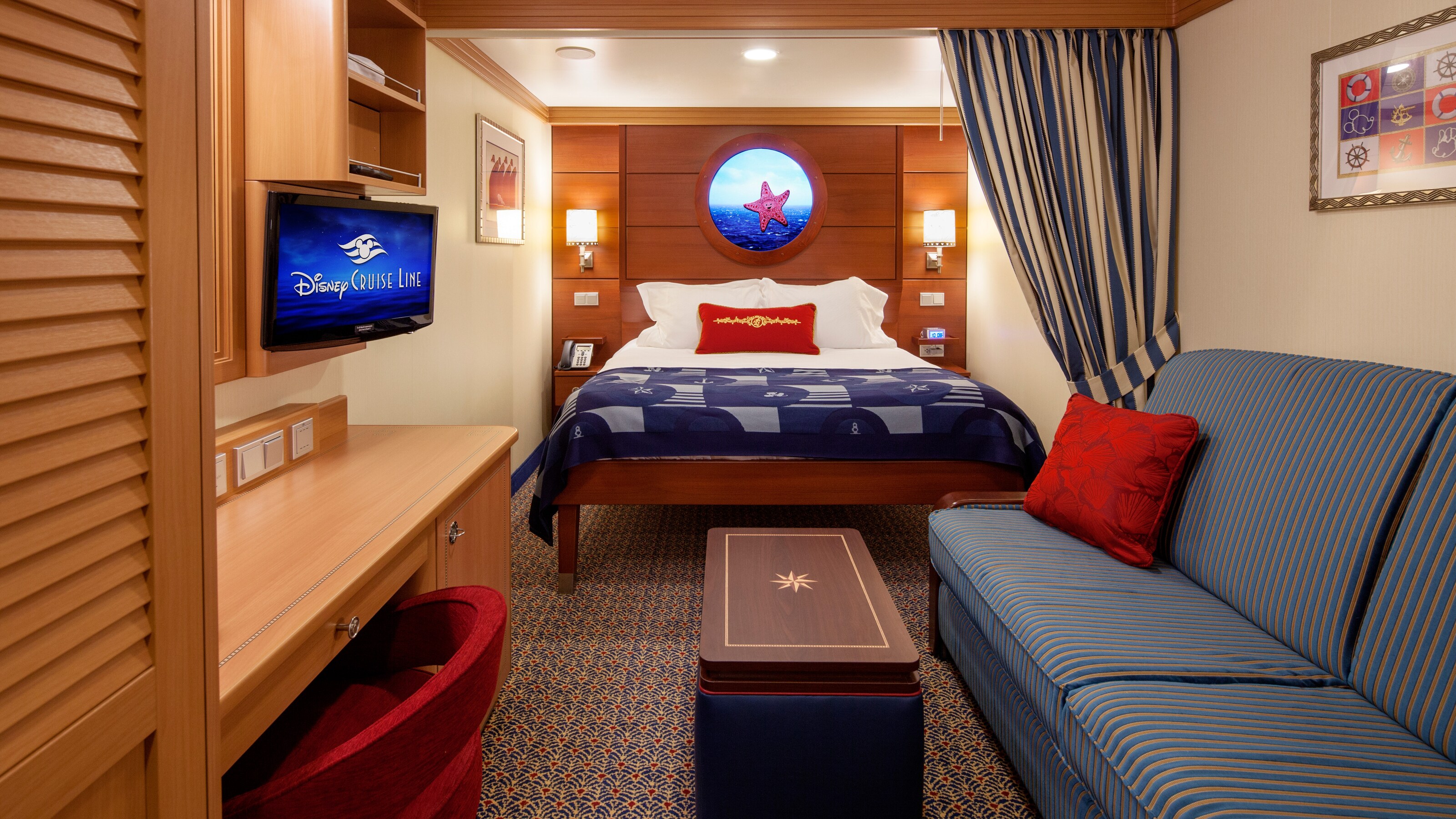 A Disney Cruise Line Standard Inside Stateroom with a desk, a TV, a bed, a virtual porthole, a sleeper sofa and a low table