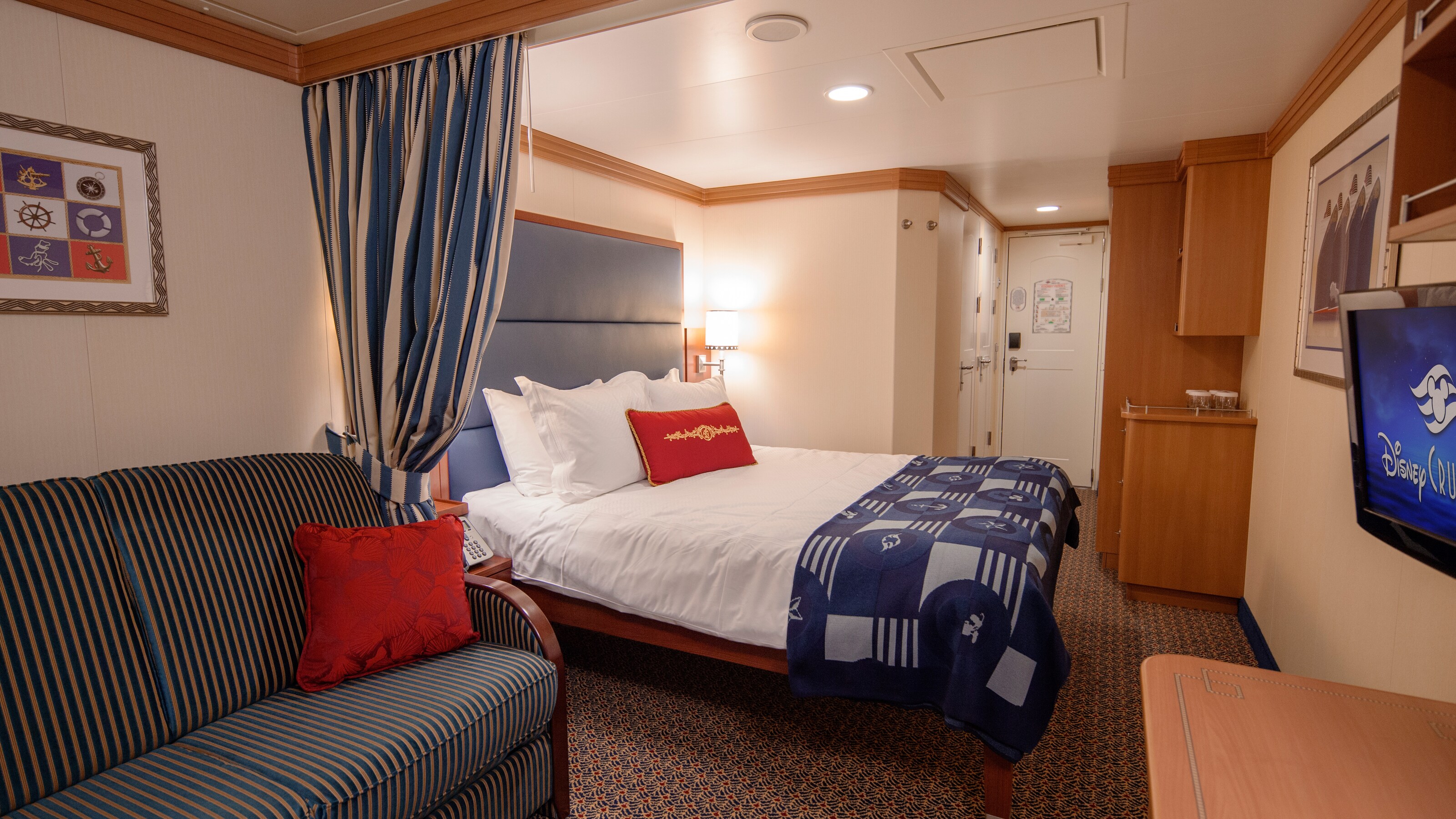 A Disney Cruise Line Deluxe Oceanview with Verandah Stateroom with a sleeper sofa, a bed, storage shelves, a TV and a desk