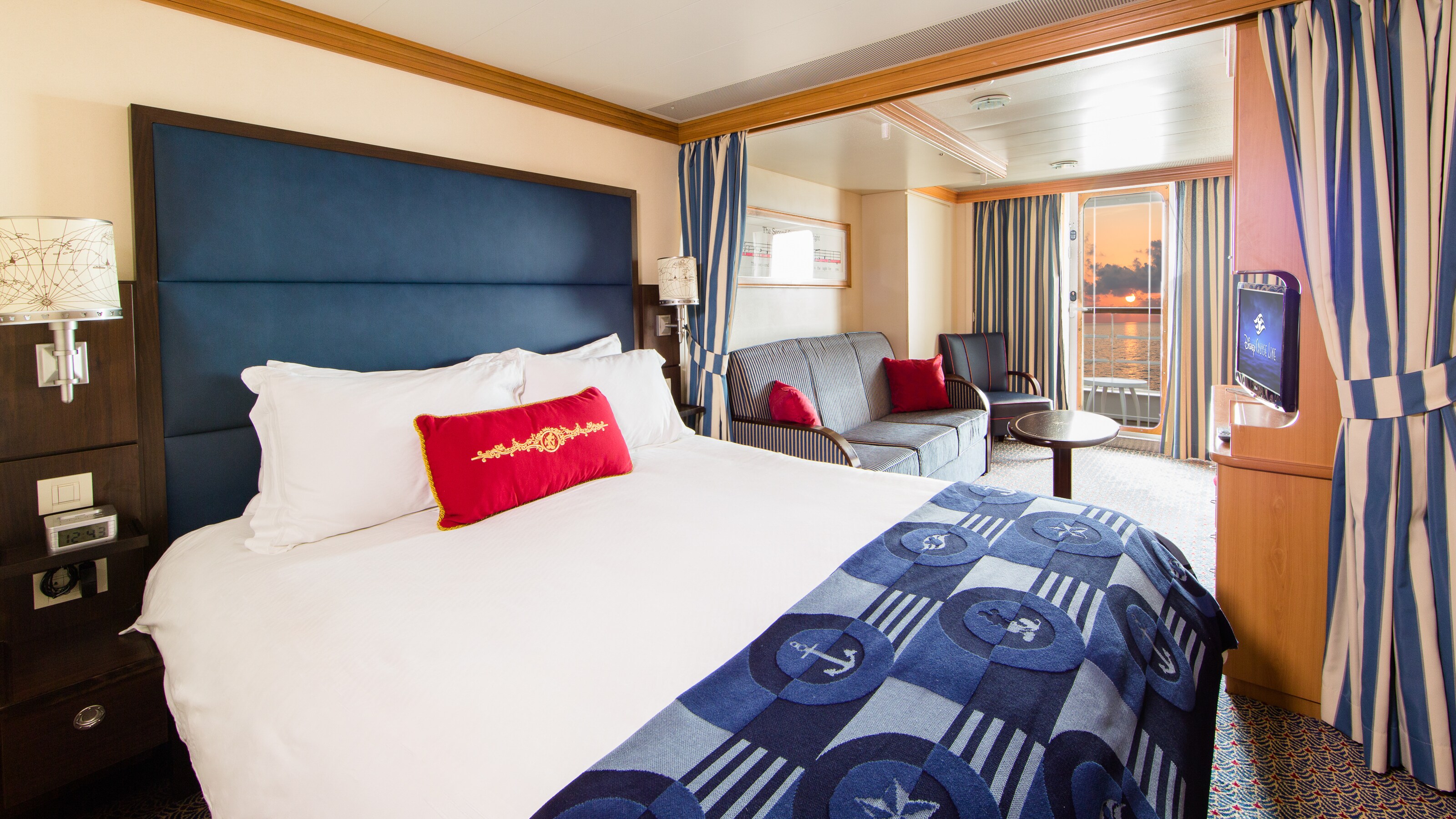 A Disney Cruise Line Deluxe Family Oceanview with Verandah Stateroom with a bed, sofa, chair, table, desk, TV, 2 nightstands and a verandah facing the ocean