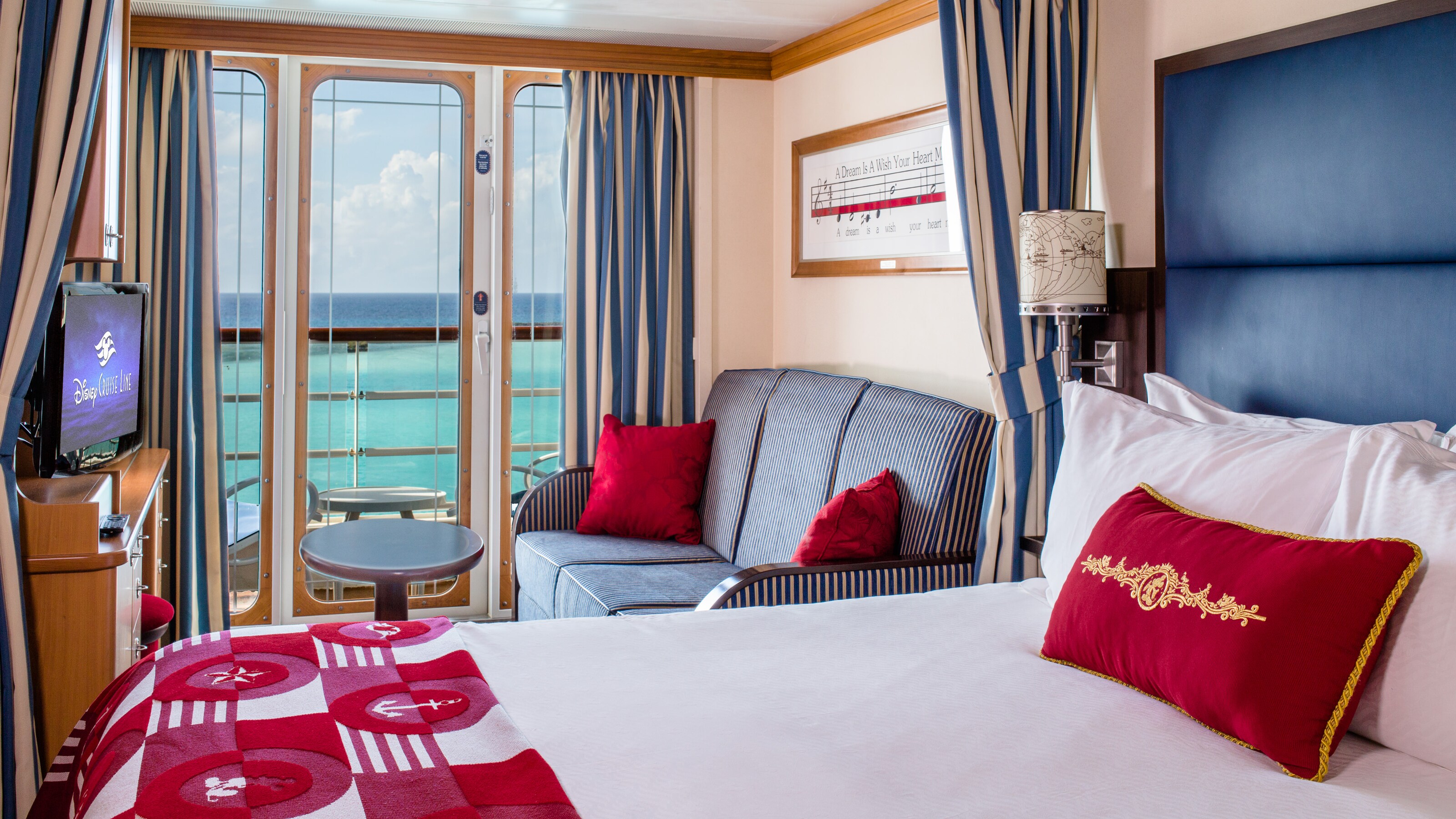 A stateroom with a queen bed, sofa, TV and verandah  