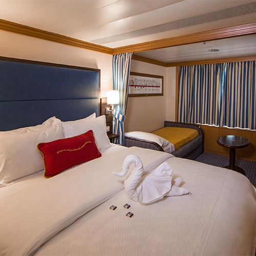 A swan towel on a queen bed, a lamp, a privacy curtain, a sofa bed and a window with closed curtains