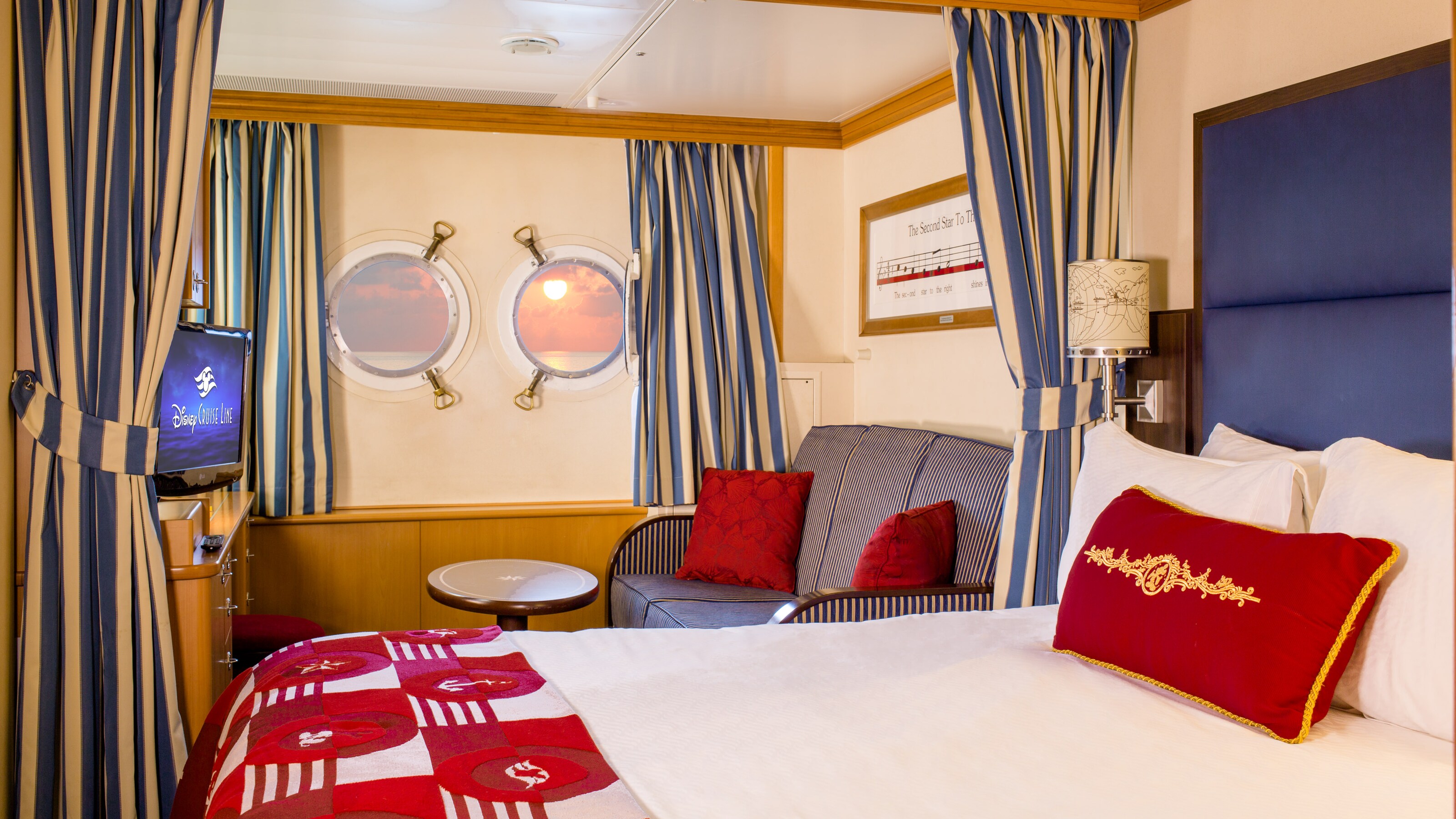 A stateroom with a queen bed, privacy curtains, sofa, TV and 2 portholes 
