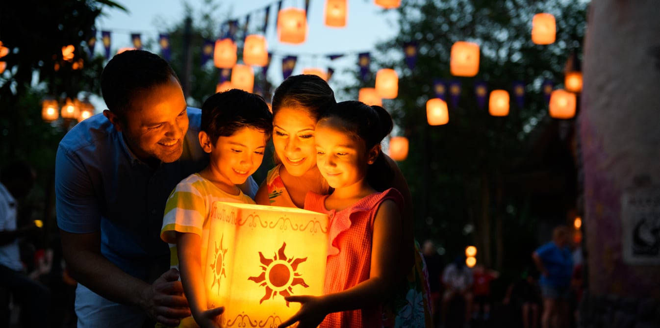 A mother, father, son and daughter gather around a luminaria latern decorated with a sun shape.