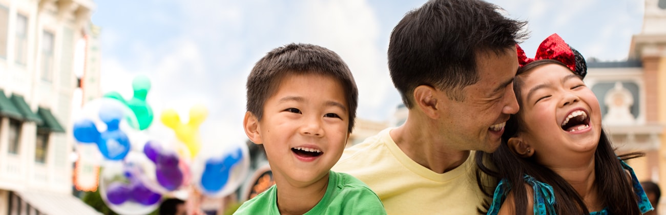 A father shares a laugh with his young son and his daughter who wears Minnie Mouse Ears and bow.