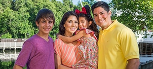 A family portrait, with mom, dad, their teen age son, an his little sister wearing a Minnie Mouse red bow and mouse ears.