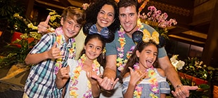 A mom, a dad, and their three kids pose for a family portrait at the Polynesian Resort wearing leis.