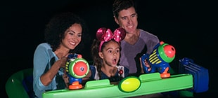 A couple and their young daughter, who is wearing a Minnie Mouse bow,  enjoying Buzz Lightyear's Space Ranger Spin shooting-gallery attraction ride.