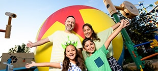 A mom and dad posing with their son and daughter in front of a big yellow Toy Story Ball designed to make guests appear the same size as toys.