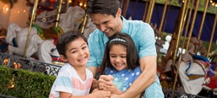 Two smiling kids try to help their dad pull the sword from the stone in front of the King Arthur Carrousel.