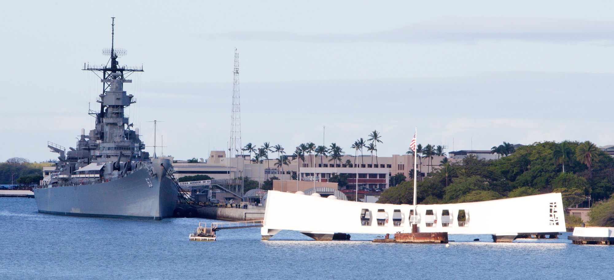 At Pearl Harbor, Hawaii, the broad geometric U S S Arizona Memorial is situated in the water beside the battleship U S S Missouri, which is docked at the pier