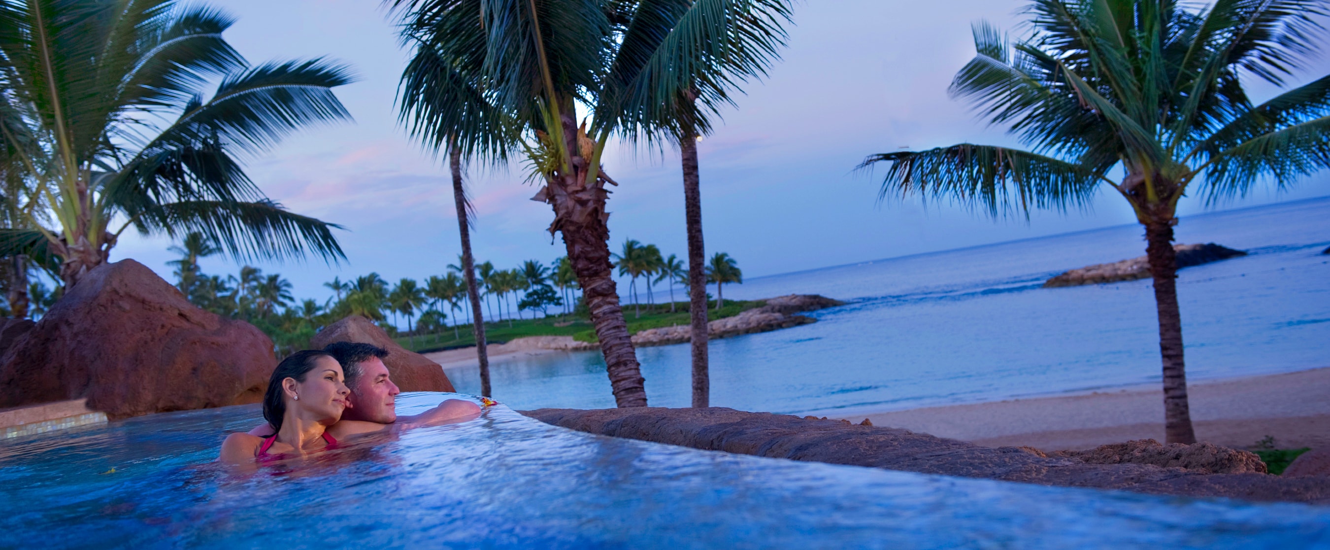 With the beachfront in the background, a couple lounges together in the adults only whirlpool spa at Alohi Point of Aulani Resort and Spa