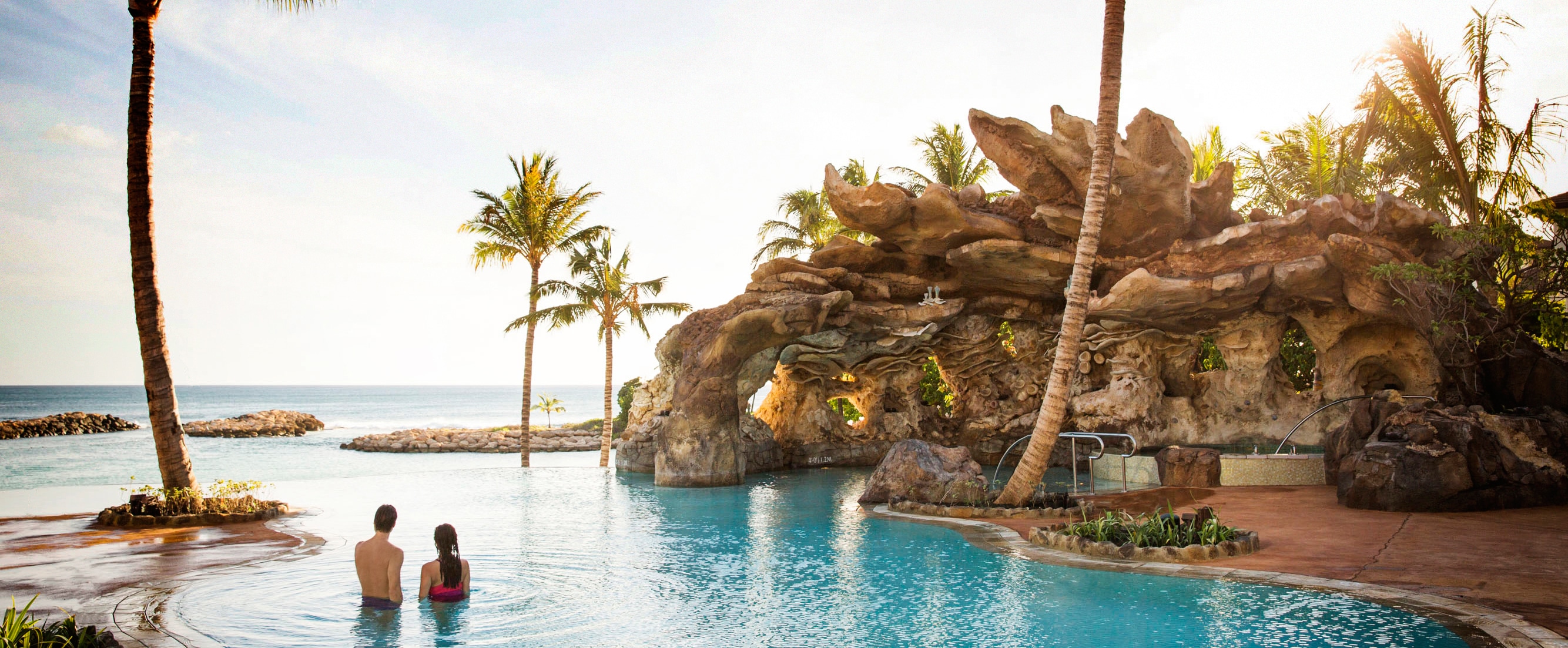 A couple unwinds in the waters of the Ka Maka Grotto oceanfront pool while looking out to the ocean