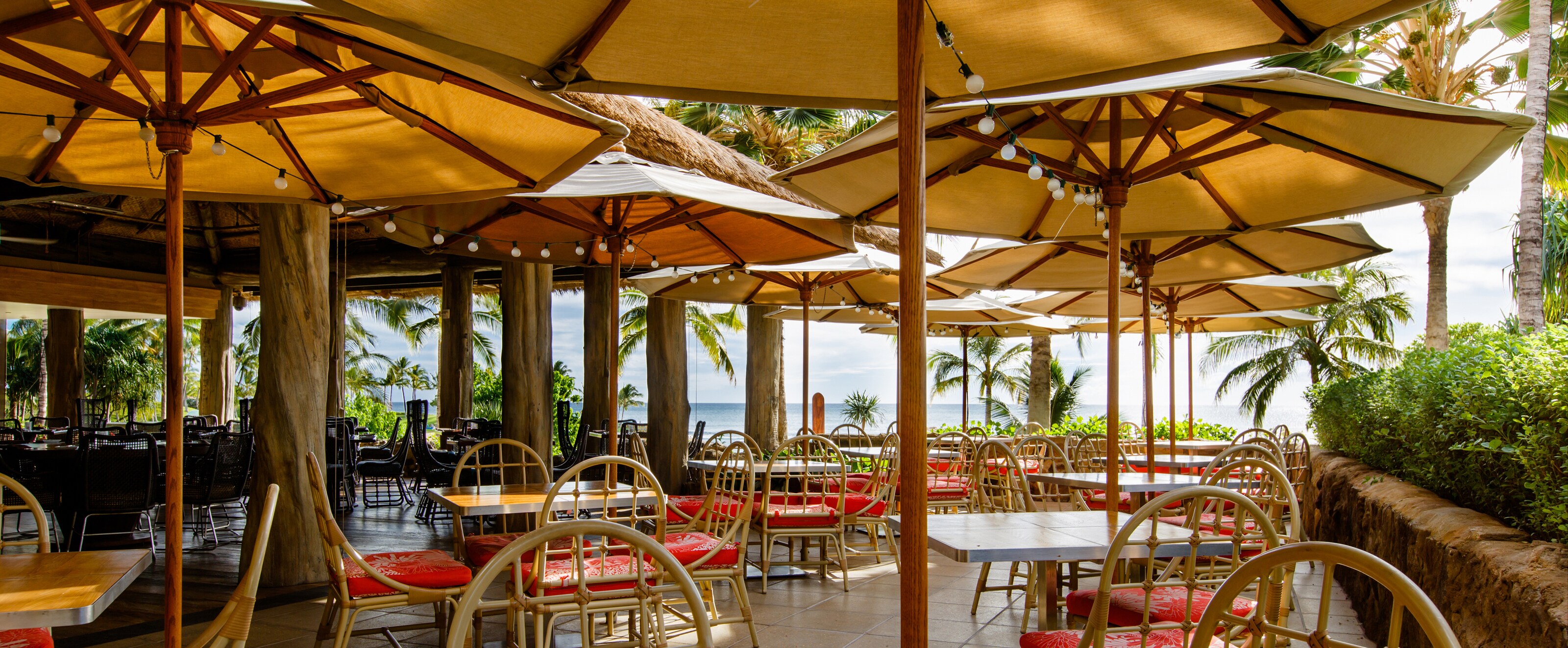 Amaama Hawaiian Cuisine Restaurant Aulani Hawaii Resort Spa Umbrellaed Outdoor Tables Strung With Lights During The Daytime Bordered By A Retaining Wall And