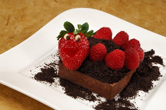 The Worms & Dirt Tart Topped with a Smiling Strawberry, Fresh Raspberries, and Chocolate Cookie “Dirt” Crumbs