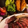 Double Joint Cowboy Cut Rib-Eye Steak served with roasted veggies, duck fat fries, salad and sauces from Raglan Road