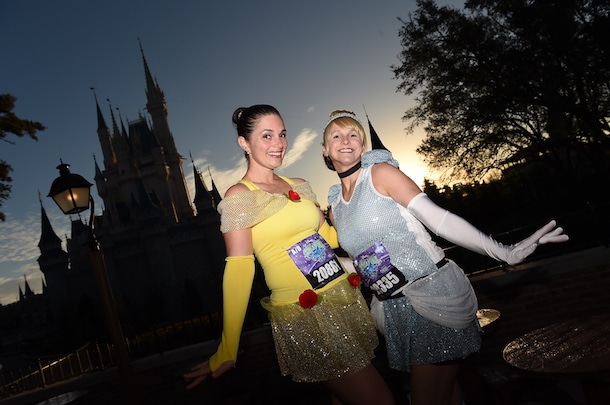 Belle and Cinderella inspired costumes for runDisney marathons pose in front of the Magic Kindgom Park
