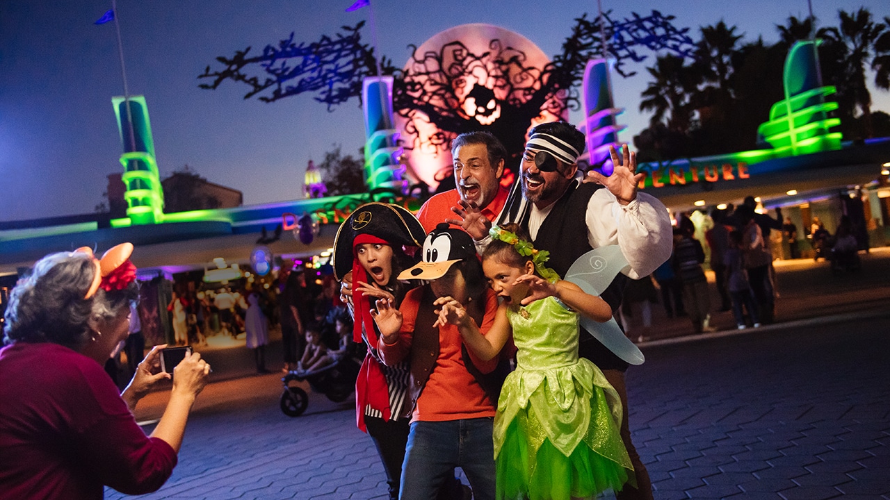 a family in costume taking a funny photo at night in front of the Disneyland entrance