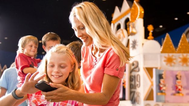 Mom and daughter look at smartphone in the queue for it's a small world at Magic Kingdom Park