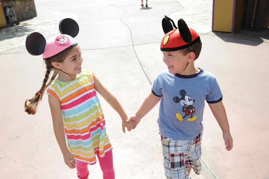 Two kids wearing Mickey ears hold hands 