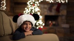 Child wearing a Santa Mickey hat in front of a Christmas Tree