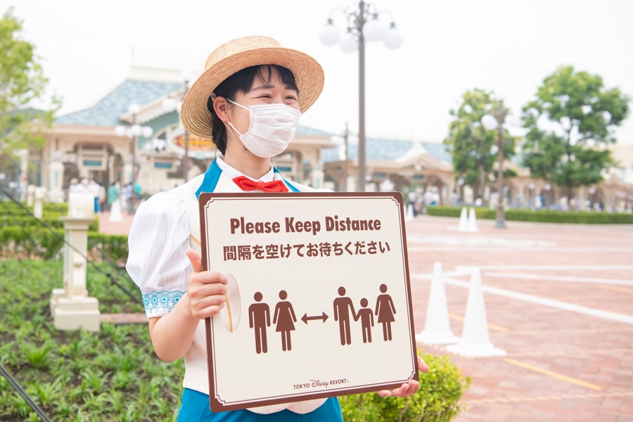 Tokyo Disney Resort cast member holds social distancing sign