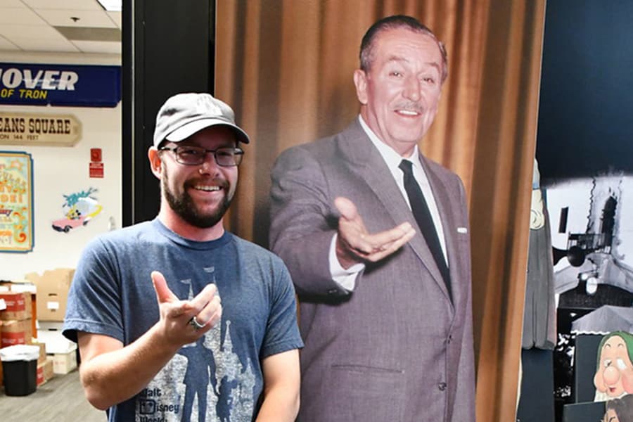 Cast member Ben poses in front of a photo of Walt Disney in the Reading Room of the Walt Disney Archives