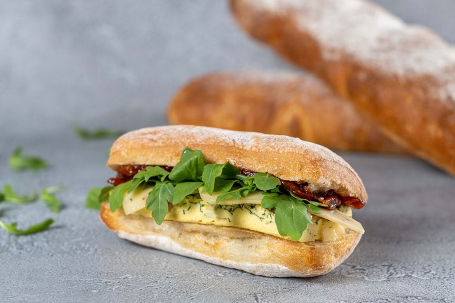 Plant-based Ciabatta Sandwich with “egg” Florentine, plant-based cheese, tomato jam, and arugula.
