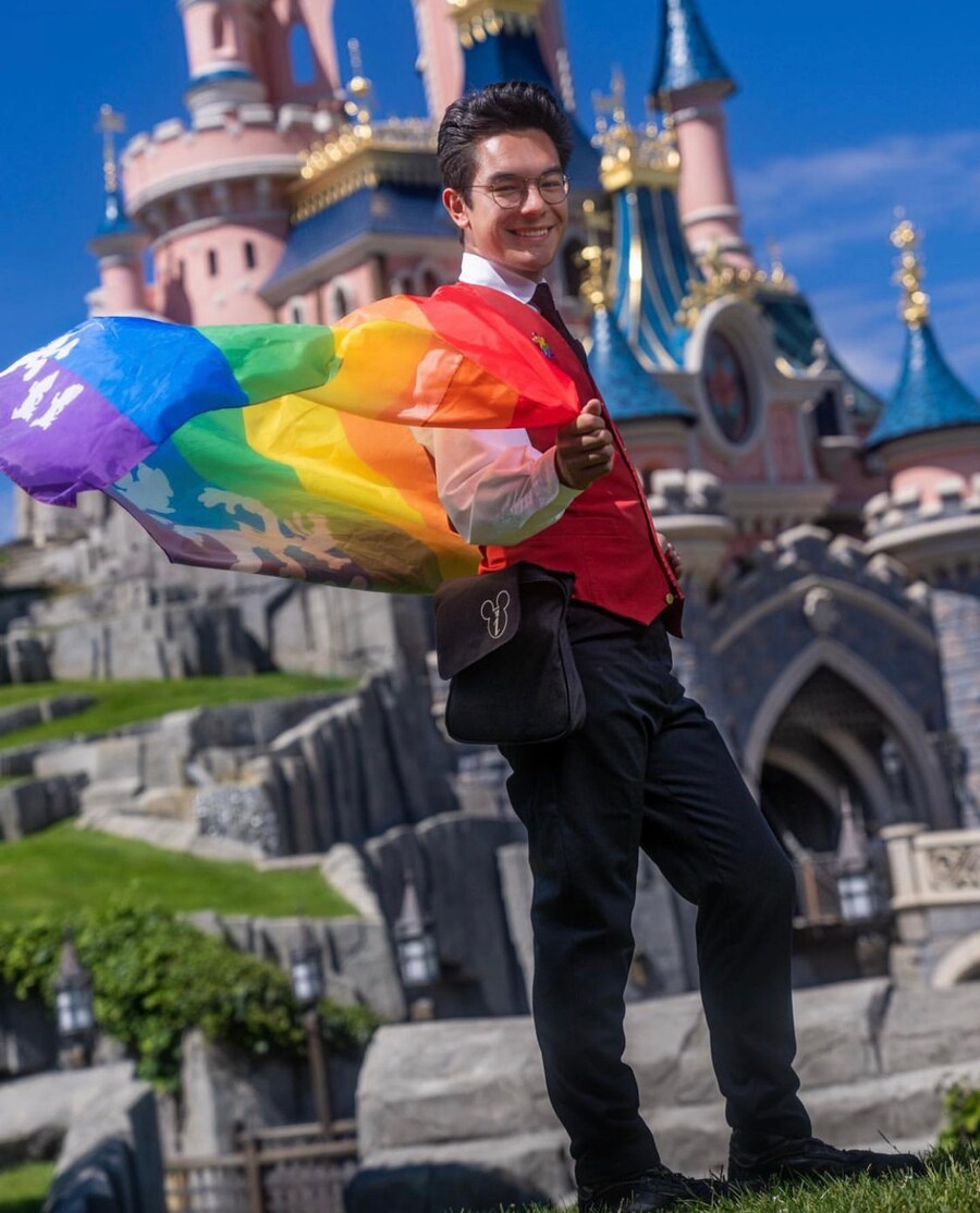 Disneyland Paris cast member in front of castle with Pride flag