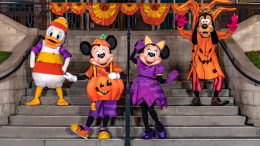 Mickey Mouse as a jaunty jack-o-lantern, Minnie Mouse as a stylish witch, Goofy as a haunted apple tree, Donald Duck as a quirky candy corn