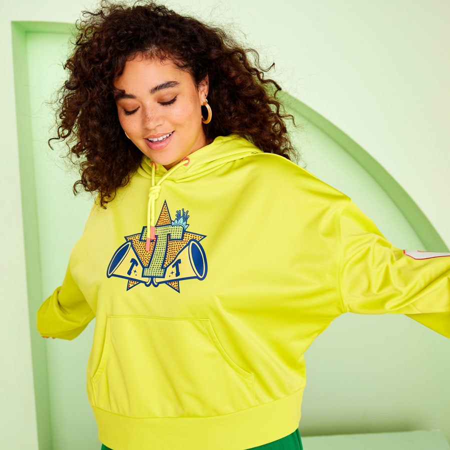 A woman wearing a yellow hoodie with a bedazzled "T" on it. 