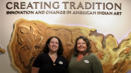 Deb Van Horn and Jackie Herrera in front of Creating Tradition: Innovation and Change in American Indian Art sign