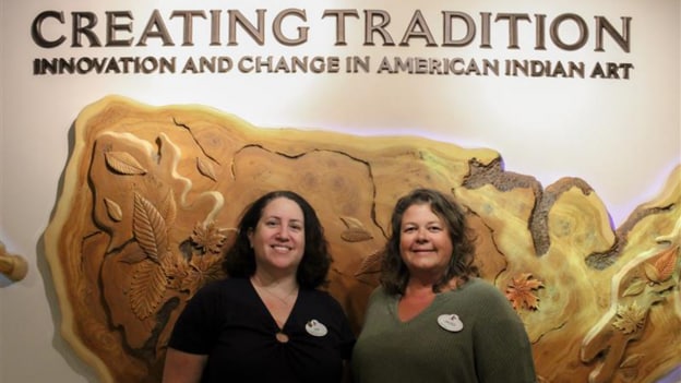 Deb Van Horn and Jackie Herrera in front of Creating Tradition: Innovation and Change in American Indian Art sign