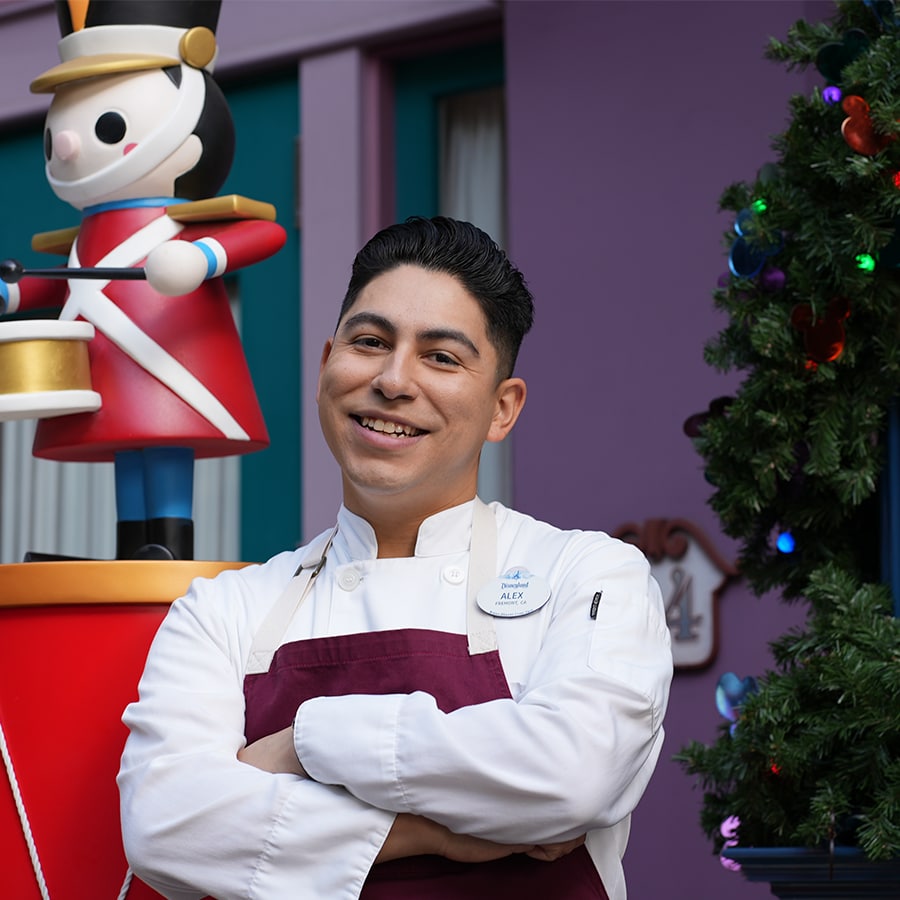 Alex stands in chef's uniform with arms folded