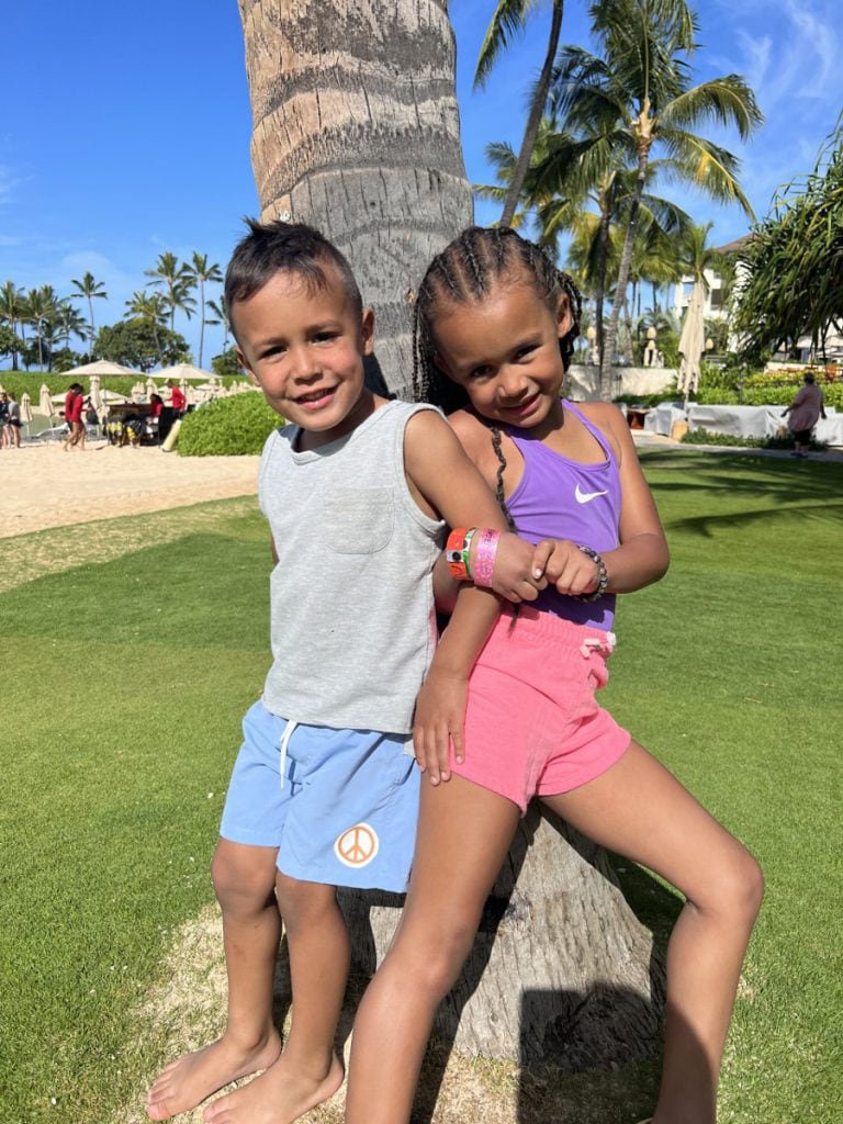 Ashely's two children enjoying a day at the beach posing in front of a palm tree behind Aulani Resort.