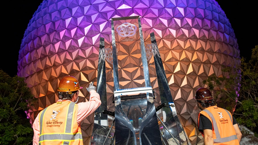 Imagineers installing new EPCOT logo pylons on entrance fountain near Spaceship Earth