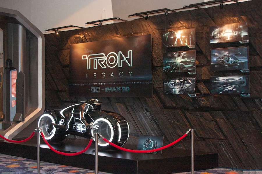 Lightcycle from “TRON: Legacy” on display at D23 Expo 2009 in front of a wall containing concept artwork from the film and the film’s logo.