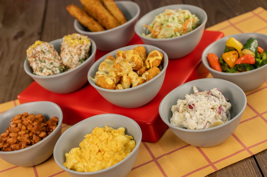 Individual bowls of The Married Spuds, Force Field Fried Pickles, Slinky Doooooooooog Mac & Cheese, Buckin’ Baked Beans, Cowpoke Corn on the Cob, Mean Old Potato Salad, Veggie Slaw, and Campfire-roasted Vegetables